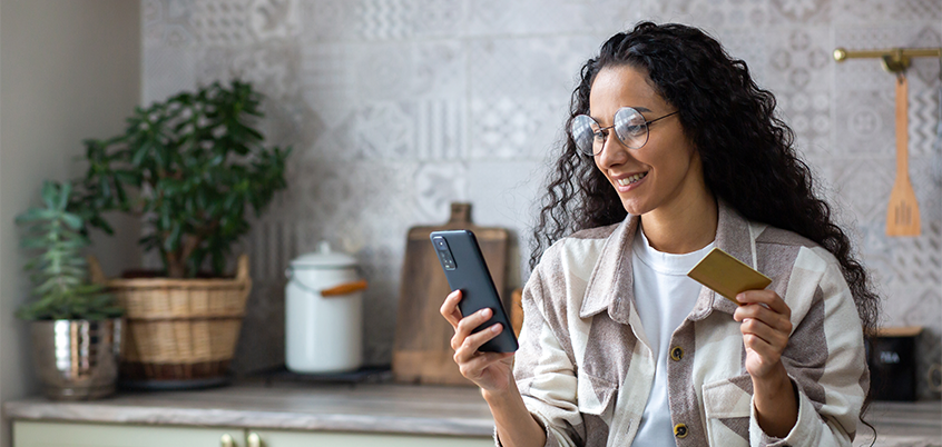 woman looking at smart phone while holding bank card
