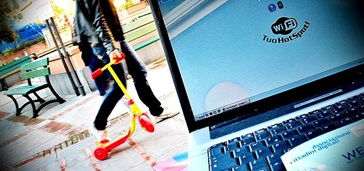 Carrier opportunities_Hero laptop using outdoor hotspot, man with child's scooter in background