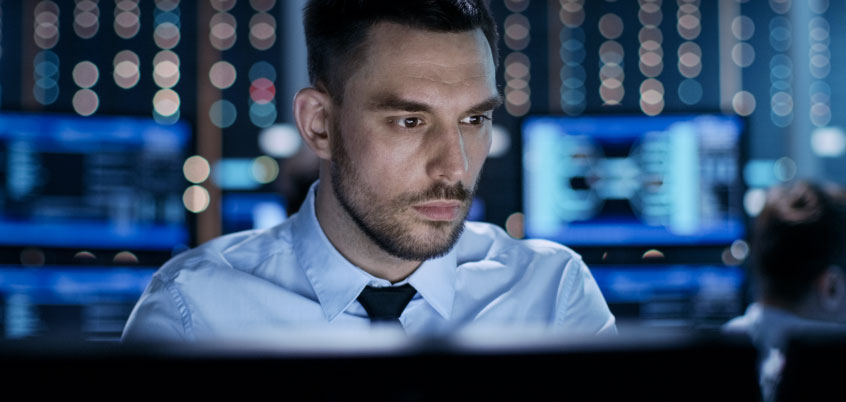 Man in front of computer screen, other screens in background