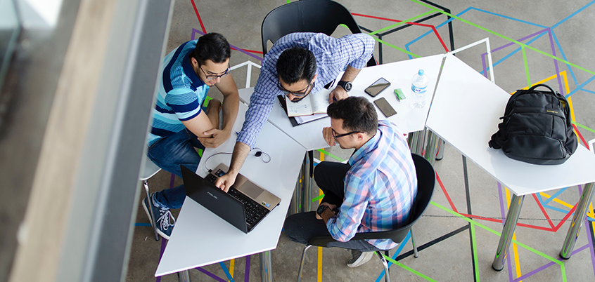 overhead shot of three men working at a desk with laptop