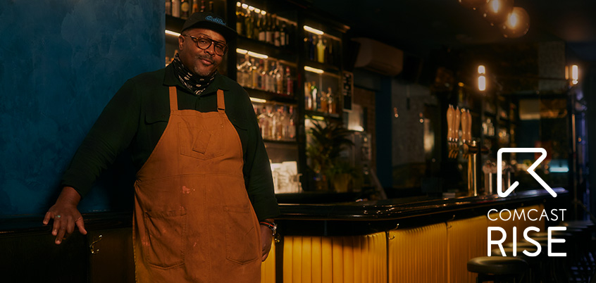 Bartender standing at counter with Comcast RISE logo.