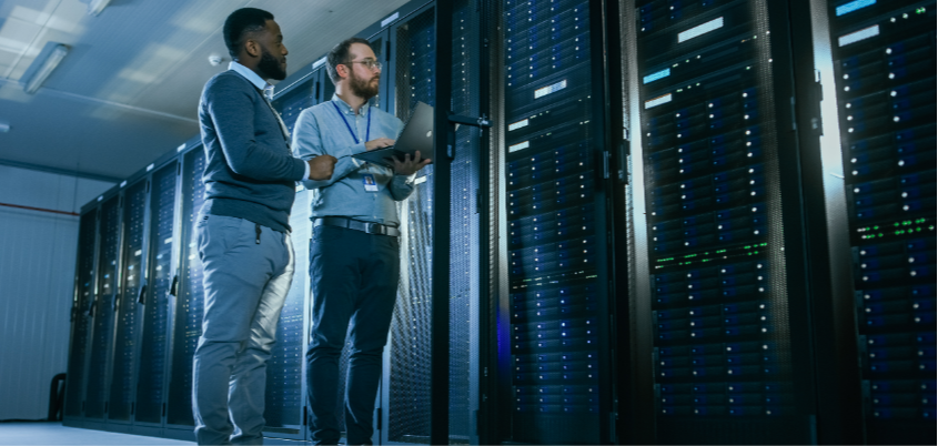 Two men standing in front of server with laptop